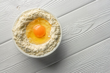 Broken egg in a bowl with flour on a wooden table.