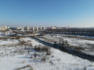 Obraz premium Urban winter landscape from above. Multi-storey buildings and trees in the city park are visible. River flows.