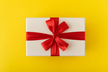 White gift box with red ribbon. Presentation on yellow background top view.
