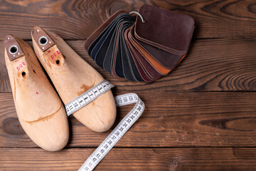Leather samples for shoes and wooden shoe last on dark wooden table. - obrazy, fototapety, plakaty