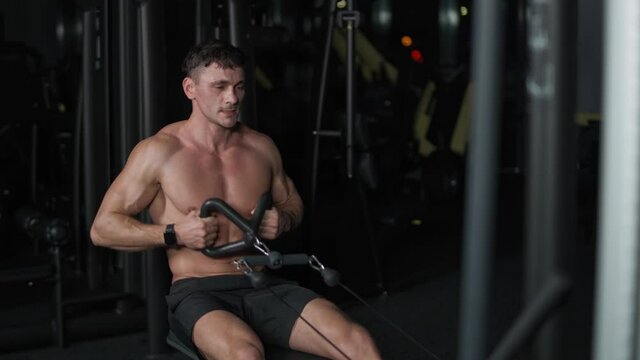 Athletic man in the Gym lifting blocks on rowing machine, training on block device and gym equipment, night time, 4k Slow Motion.