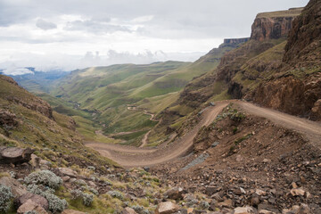 Steep winding mountain road of Sani Pass between South Africa and the Kingdom of Lesotho border controls under cloudy sky