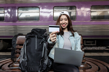 Attractive young Asian backpacker woman with credit card at train station. Ready for travel.