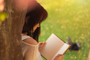 Close up of young women was look at a book in hands under a tree in the park during the holidays. summer time. Activity on weekend.