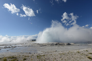 A small geyser at Yellowstone National Park erupting on a sunny day with a few clouds