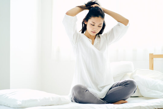 ベッドの上で髪を結う30代日本人女性