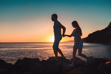 Fototapeta premium Summer holiday and lovers. Silhouette of a young couple running along the beach. Side view