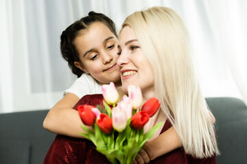 Woman and child with bouquet of flowers against home background. Spring family holiday concept. Women's day
