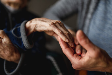 Unrecognizable young person holding hands of old woman. Elderly, care, family concept