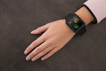 Woman measuring oxygen level with smartwatch at grey table, top view
