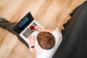 Top view of a young male programmer drinking coffee and writing on a laptop keyboard. The concept of people working with technology and computer at home