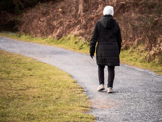 Senior woman in white hat and black jacket walking in a park on a small path. Healthy activity for elderly concept