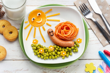 Fun Food for Kinds - Cute smiling snail made of a hotdog and spaghetti served with green peas and cheddar cheese. Creative cooking for children