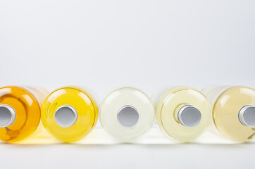 Collection lying transparent bottles with different pale colors liquid, cosmetic product, perfume or drink and blank silver cap on white background as decorative border, front view, closeup.
