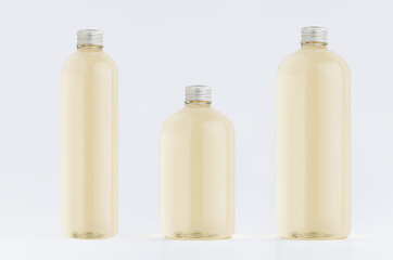 Assortment of three plastic tall, low and thick bottles with pale fresh drink or cosmetic essential oil, silver cap mockup on white background, template.