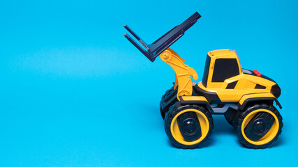 The yellow black forklift toy typewriter on a blue background. Construction equipment tractor for...