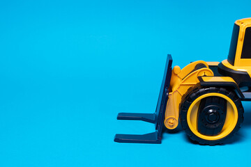 The yellow black forklift toy typewriter on a blue background. Construction equipment tractor for children for toy store, copyspace place for text
