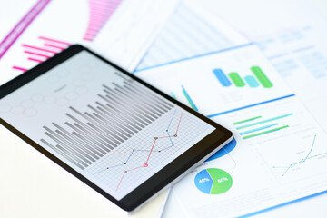 Tablet with graphs lying on documents in office closeup