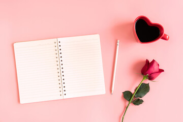 Valentine's Day background. Heart shaped cup of black coffee, red rose and notebook on pastel pink background. Valentine day concept. Flat lay, top view, copy space