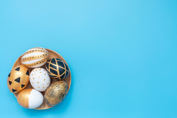 Top view of easter eggs colored with golden and black paint in differen patterns on blue background. Minimal easter concept. Flat Lay of Golden Easter Eggs. Copy space.
