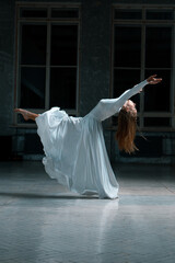 girl pulls her leg forward with backward bending, beautiful dance pose, contemporary in white dress, ballroom movements.