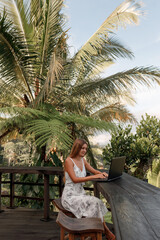 Fototapeta na wymiar Freelance concept. Pretty young woman using laptop in cafe on tropical beach in outdoor cafe terrace. Work and travel