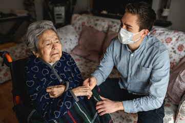 old sick aged woman in wheelchair. Family, home care concept. Man with protective mask