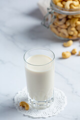 Vegan cashew milk in glass with cashews nuts on marble background