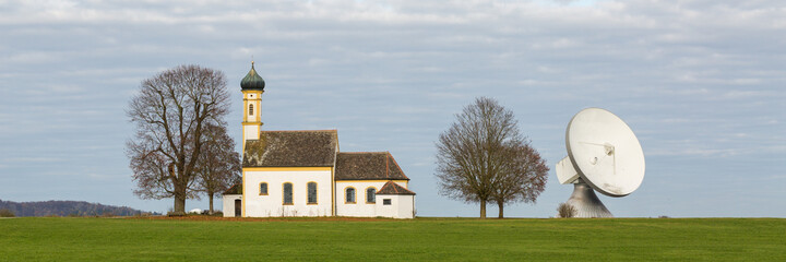 Raisting, Germany - Nov 13, 2020: Panorama with a church and a satellite dish (radome). Symbiosis...