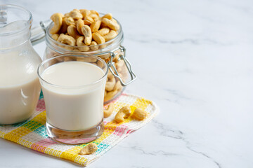 Vegan cashew milk in glass with cashews nuts on marble background