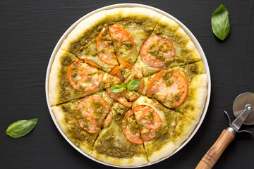 Homemade Pesto Pizza with Fresh Tomatoes and Mozzarella on a black background, top view. Flat lay, overhead, from above.