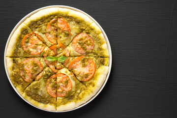 Homemade Pesto Pizza with Fresh Tomatoes and Mozzarella on a black background, top view. Flat lay, overhead, from above. Copy space.