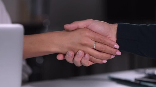 Man and woman shake hands during corporate business meeting in modern office spbi. Closeup view of businessman and businesswoman shaking arms and working together at desk with laptop in light interior