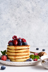 Pancakes with berries and maple syrup for breakfast on a light background.