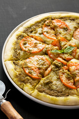 Homemade Pesto Pizza with Fresh Tomatoes and Mozzarella on a black background, low angle view.