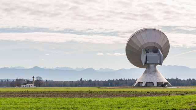 Backside view on a satellite dish of the Raisting Radome. In the distance the silhouette of mountains (alps) and a church.