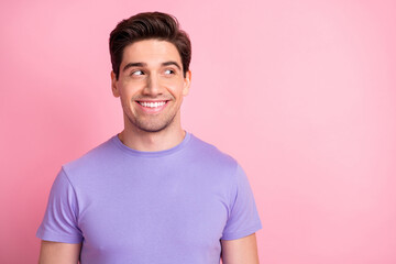 Portrait of attractive cheerful guy wear violet tshirt looking aside copy space isolated over pink pastel color background