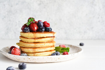 Pancakes with berries and maple syrup for breakfast on a light background.