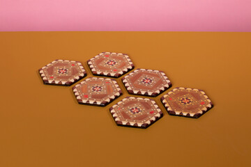 Vintage marquetery inlayed coasters with brown and beige colors. An eclectic oriental pattern made from mosaic wood on an ochre table and a pink background. Horizontal