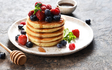 Pancakes with berries and maple syrup for breakfast on a dark concrete background.