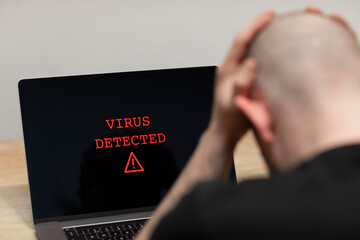 Virus detected with a warning sign on a laptop. A desperate man sitting in front of his computer with the warning on his screen. Cybercrime, infected unsafe device