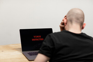 Virus detected and a warning sign in red on a laptop. A desperate man sitting in front of his...