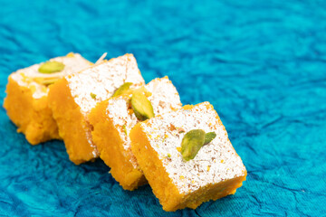 Famous Indian Mithai Moong Dal Burfi Barfee Or Meetha Mung Daal Barfi Made Of Yellow Gram Flour In Desi Ghee Mixed With Mawa Pistachio And Doodh Khoya. Blue Turquoise Background With Space For Text