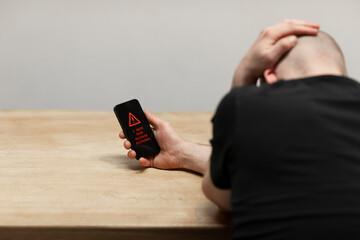 Red warning text saying ‘I have your private pictures’ on a hacked cell phone. A man, the sextortion victim holding his phone while being desperate. Cybercrime, ransomware