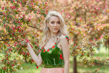 Large portrait of a blonde woman in spring in a blooming garden and in a beautiful green dress of original design