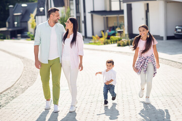 Fototapeta premium Full length body size view of four cheerful people dad mom small little kids embracing going outside enjoying leisure good weather