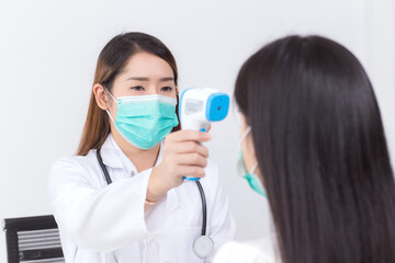 Asian woman doctor uses a infrared forehead thermometer to measure body temperature of patient,...