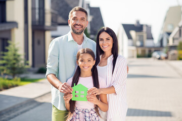 Obraz premium Photo of happy cheerful good mood smiling positive family hold little green home paper card hug each other outside outdoors