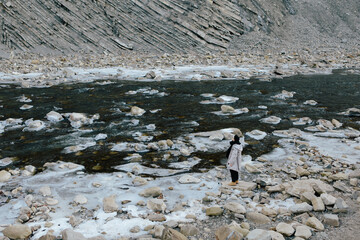 Hiker among the rocks on the bank of a mountain stream in warm clothes