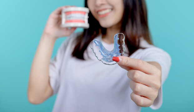 Smiling Asian woman holding orthodontic retainer on blue screen background. Dental care and healthy teeth.